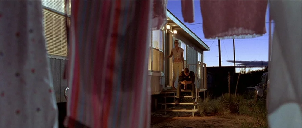 The Three Burials of Melquiades Estrada (2005) movie still: wide — A manufactured home sits in a desert-like landscape at dusk under a darkening…
