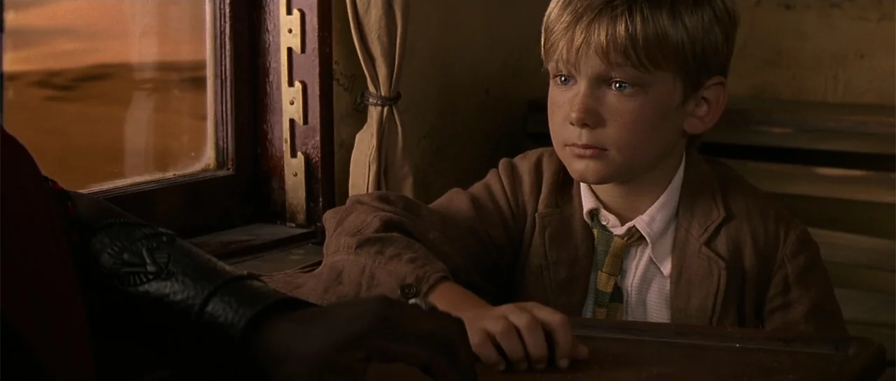 The Mummy Returns (2001) movie still: medium — A vintage wood-paneled train compartment features a window looking out at a desert landscape. A young…