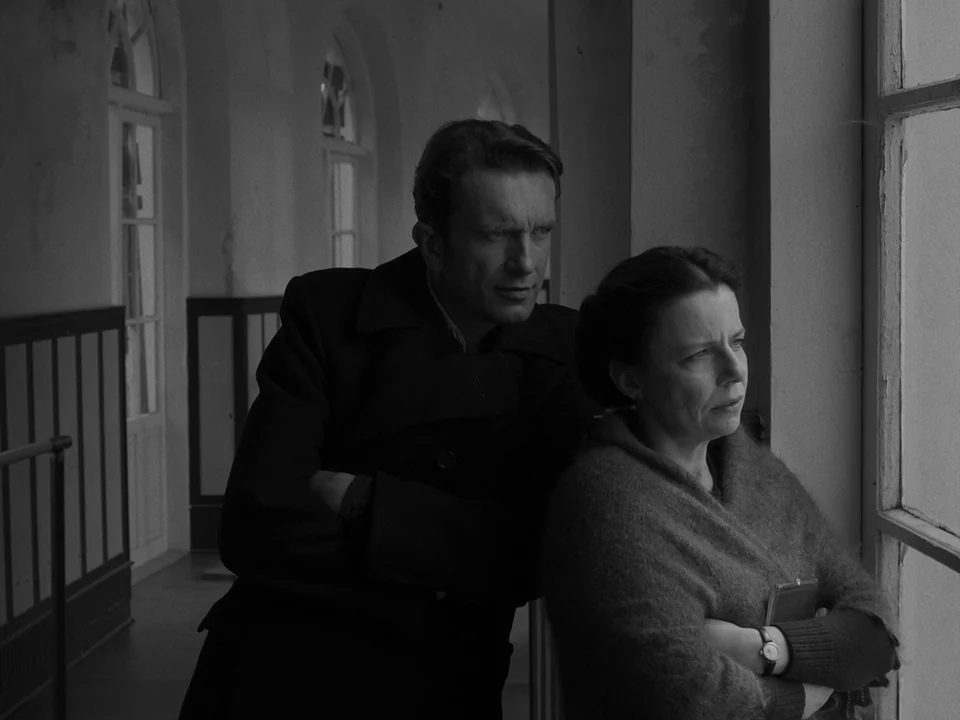 Cold War (2018) movie still: medium — A dimly lit hospital hallway features high arched windows and stark white walls. A man and a woman stand…