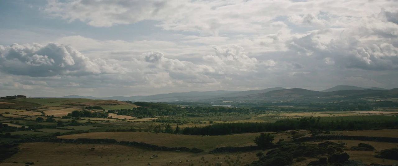 The Rhythm Section (2020) movie still: establishing — A sprawling Irish countryside features rolling hills, stone walls, and clusters of dark trees.…