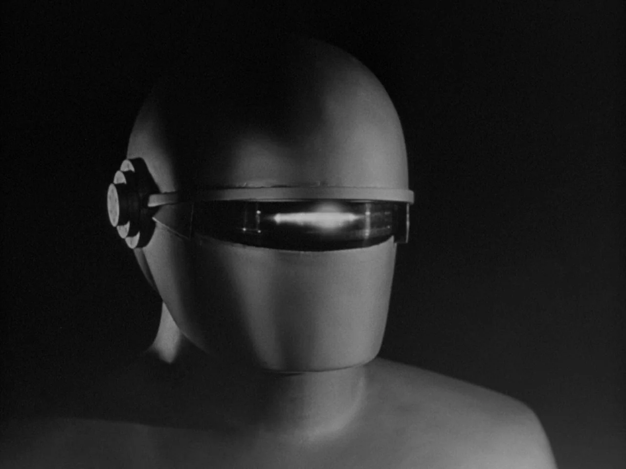 The Day the Earth Stood Still (1951) movie still: closeup — A featureless, dark space containing only a mechanical robot figure. The figure wears a…