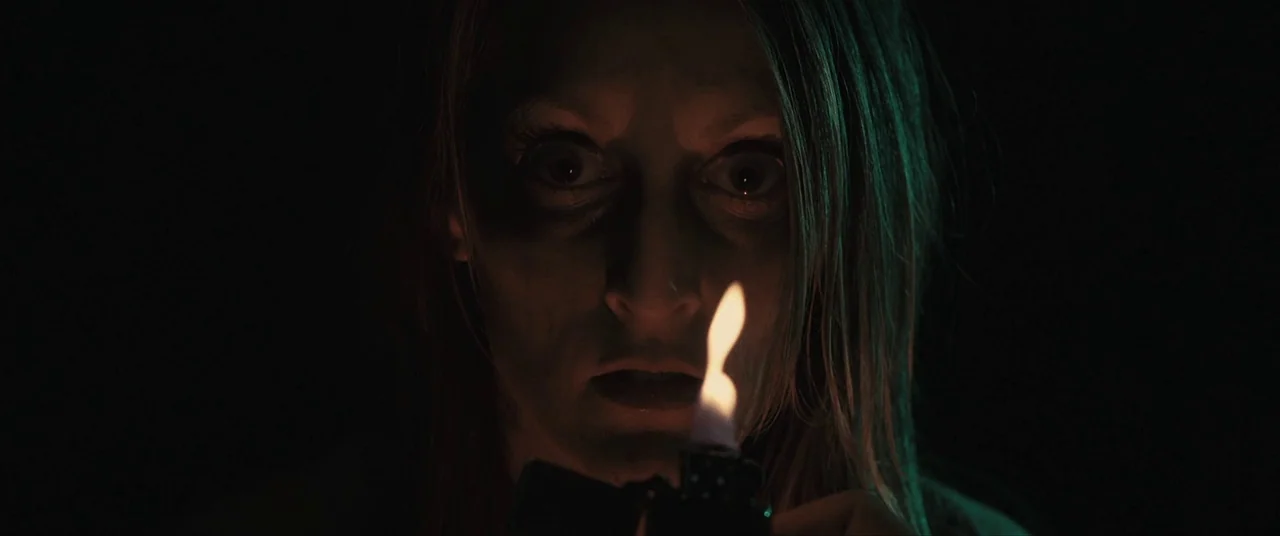 The Editor (2014) movie still: closeup — A person is in a completely dark space illuminated only by a small flame. The flickering firelight casts…