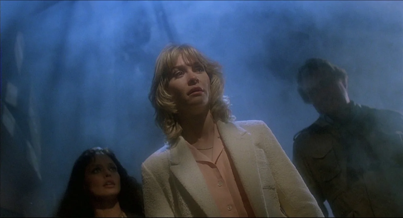 The Howling (1981) movie still: medium — A dark space filled with dense blue smoke and indistinct structural shapes. Three people stand together…