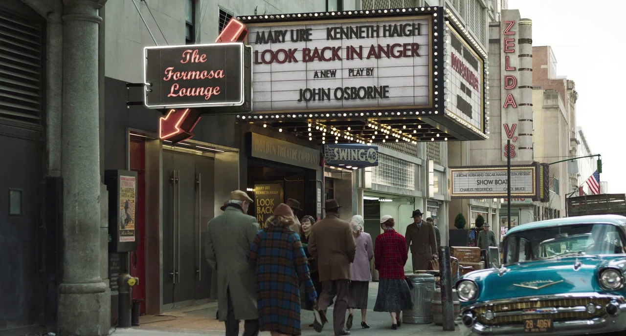 Motherless Brooklyn (2019) movie still: wide — A 1950s city street displays a marquee for the play Look Back in Anger. Pedestrians in period…