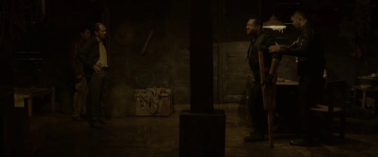 The Raid 2 (2014) movie still: wide — A dimly lit wooden structure contains ropes, wooden pillars, and scattered tools. Four men interact in the…