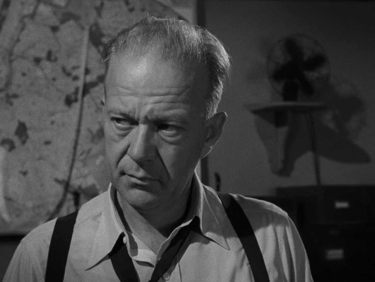 Pickup on South Street (1953) movie still: closeup — A dimly lit room contains a map on the wall and a desk fan. A middle-aged man in a dress shirt…