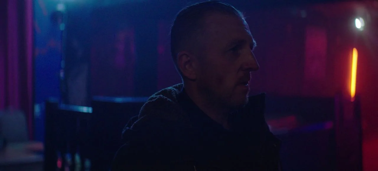 A Good Woman Is Hard To Find (2019) movie still: medium — A dark bar interior features neon lighting casting colorful shadows on the walls and…