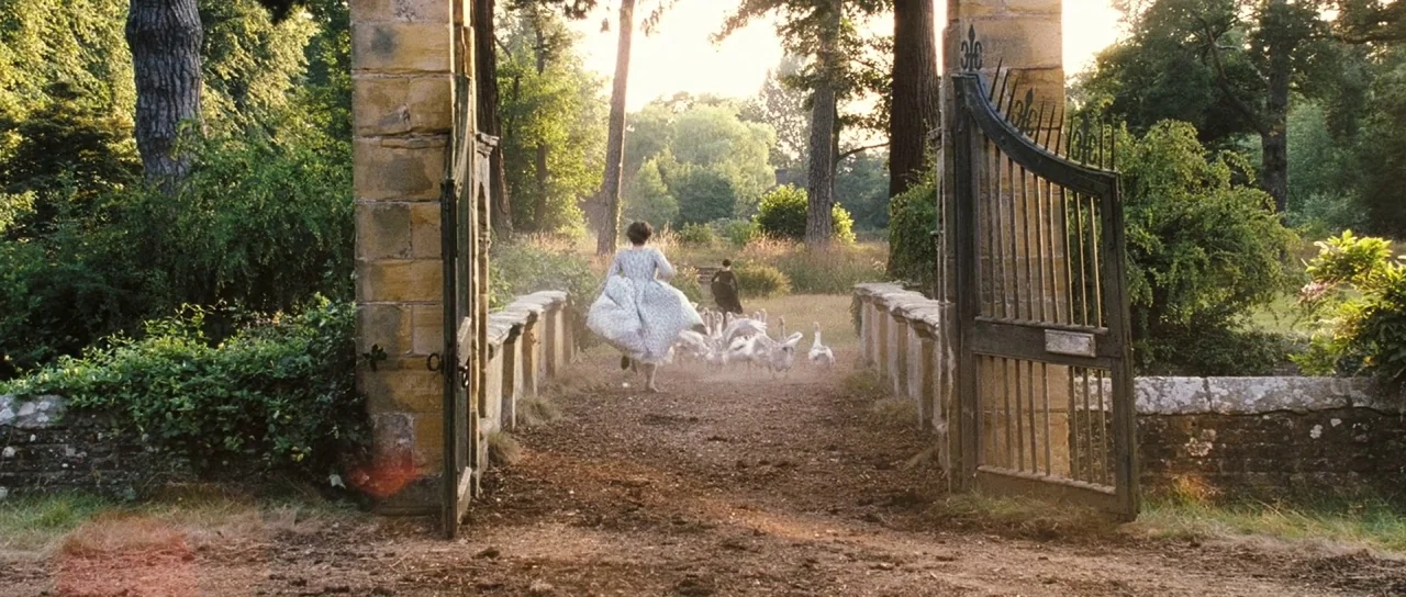 Pride & Prejudice (2005) movie still: wide — A pair of stone pillars frame a dirt pathway leading into an open estate. A young woman in a dress runs…