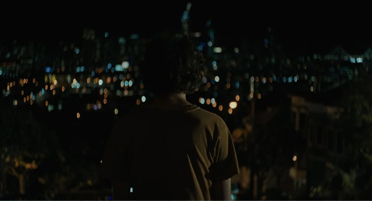 Beautiful Boy (2011) movie still: medium — A dark balcony overlooking a distant urban landscape with numerous soft-focus blurred lights. A youth…