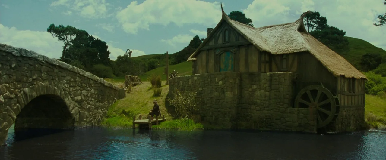 The Lord of the Rings: The Fellowship of the Ring (2001) movie still: wide — A rural fantasy watermill with a thatched roof sits beside a stone…
