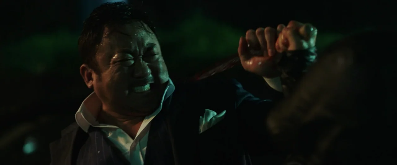 The Gangster, the Cop, the Devil (2019) movie still: medium — A dark urban outdoor setting at night with low-key lighting and blurred background…