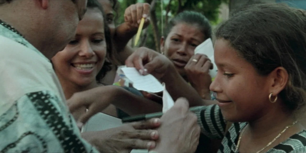 Leyenda Viva (2022) movie still: medium — An outdoor area with multiple people surrounding a man to get autographs on paper. A man signs papers held…