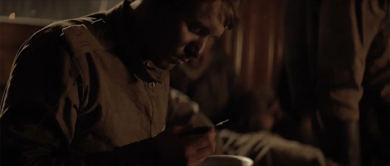 The Rifleman (2019) movie still: closeup — A dark, cramped interior space with wooden surfaces suggesting military quarters. A young man in uniform…