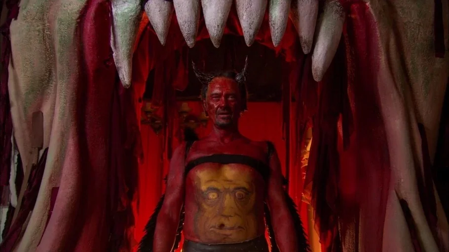 The Tudors (2007) movie still: medium — A man painted entirely in red stands within a large prop set of monster jaws. The backdrop is composed of…