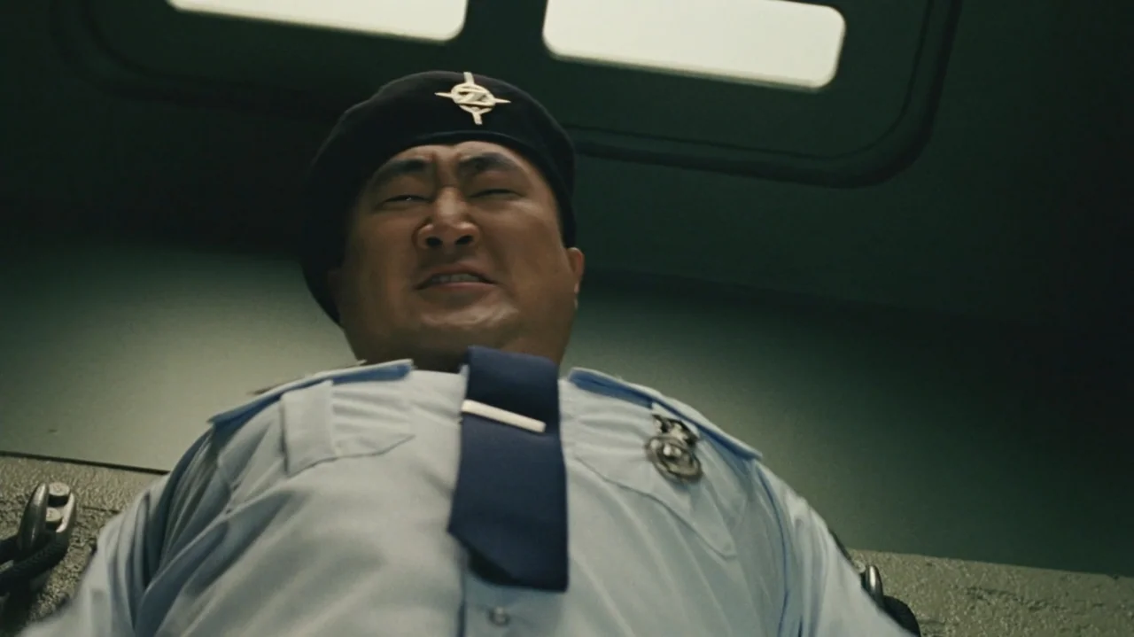 Zoom (2006) movie still: medium — An interior security booth with a green-toned wall surface visible in the background. A security guard in uniform…