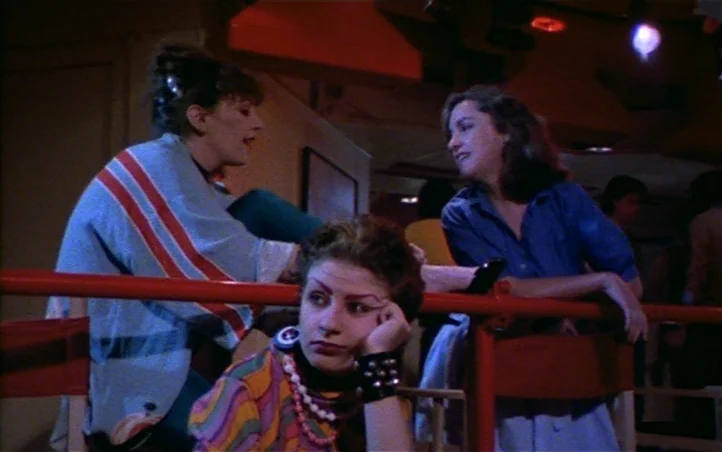 Pepi, Luci, Bom and Other Girls Like Mom (1980) movie still: medium — Three young women stand behind a red railing in a dimly lit, crowded club. One…