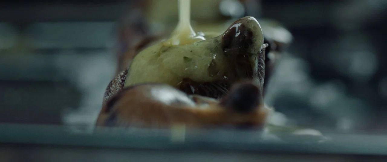 The Platform (2019) movie still: closeup — A close-up shot of a food preparation surface with a dark, blurred background. A thick yellowish sauce…