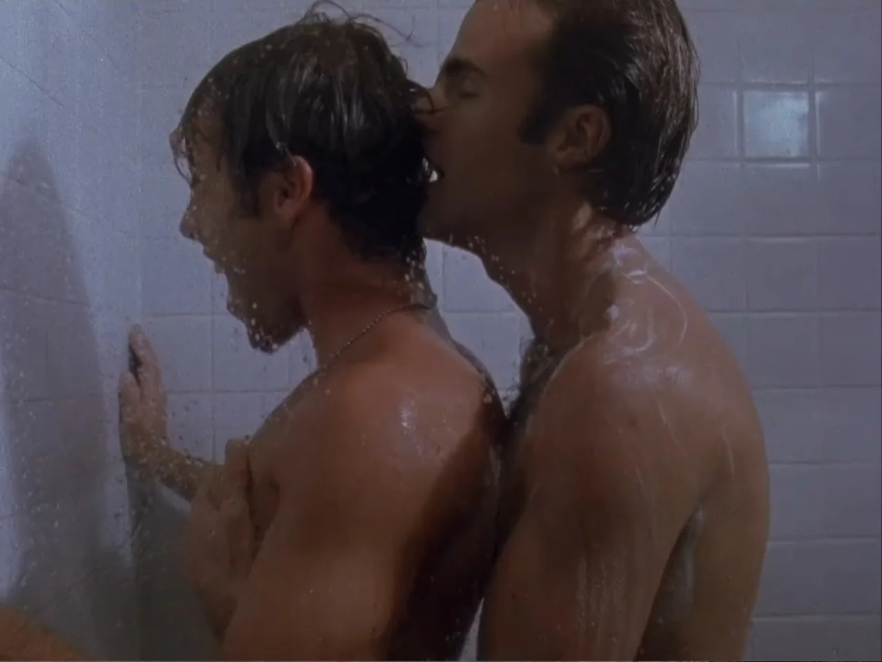 The Living End (1992) movie still: medium — A tiled shower stall interior with water spray falling over two shirtless men. Two young men stand…
