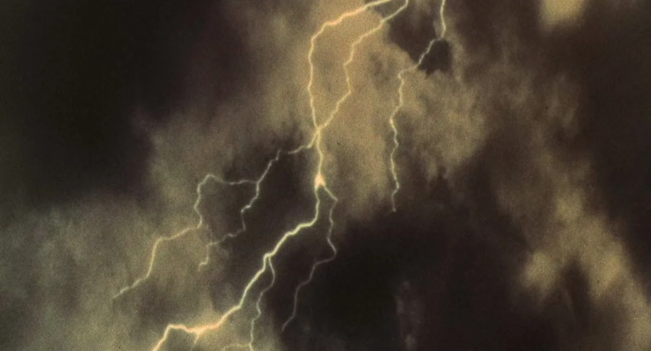 God Told Me To (1976) movie still: establishing — Dense dark storm clouds fill the frame during a night weather event. A jagged lightning bolt…