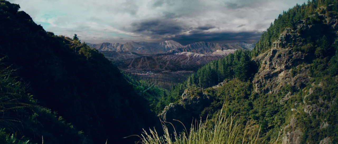 Z for Zachariah (2015) movie still: establishing — A wide mountain valley features steep rock faces covered in dense green pine trees. Dark storm…