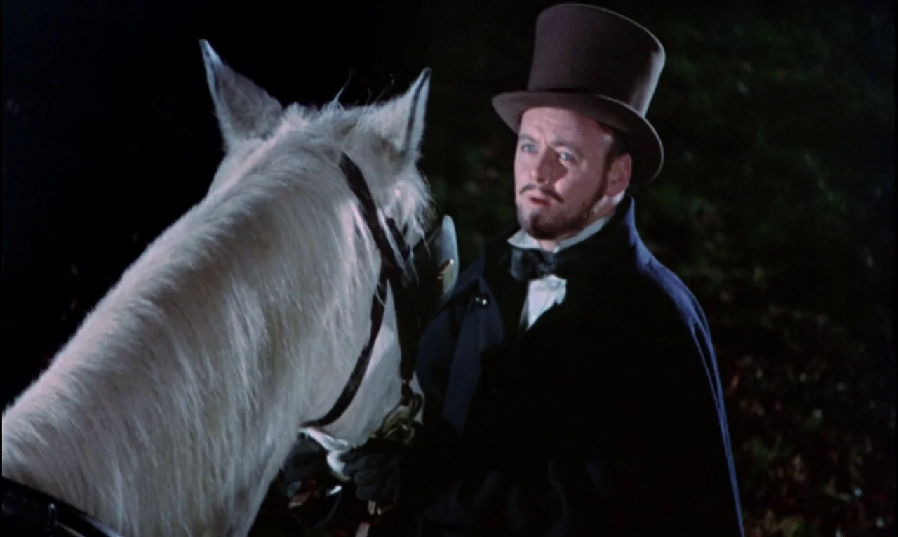 The Curse of Frankenstein (1957) movie still: medium — A dark outdoor setting at night features a man standing beside a white horse. The man wears…