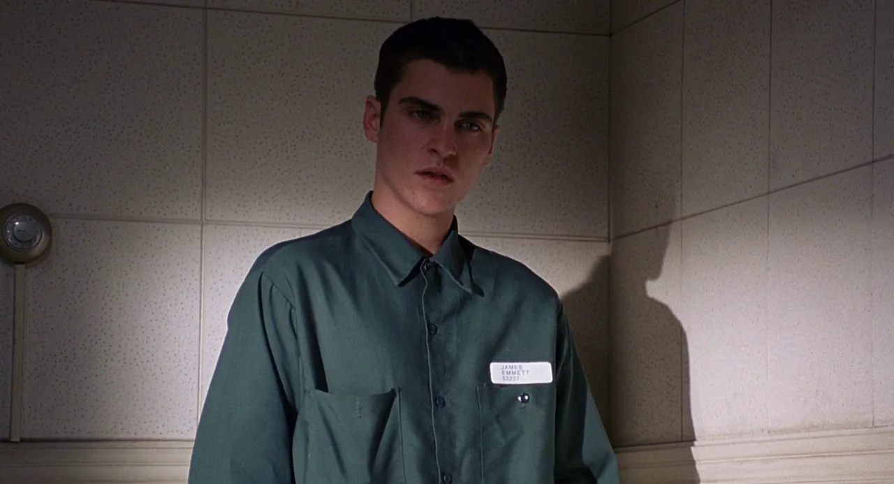 To Die For (1995) movie still: medium — A man stands against a tiled wall with a metallic thermostat visible. The person wears a dark green uniform…