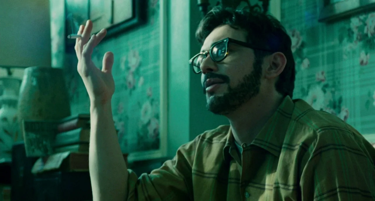 Howl (2010) movie still: medium — A domestic space features wallpaper with a vintage floral pattern under low green light. A man with a beard and…