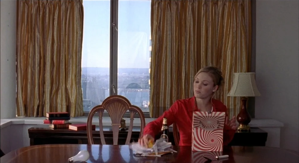 Hamlet (2000) movie still: medium — A hotel room with striped golden curtains covering a large window overlooking a city. A woman sits at a polished…