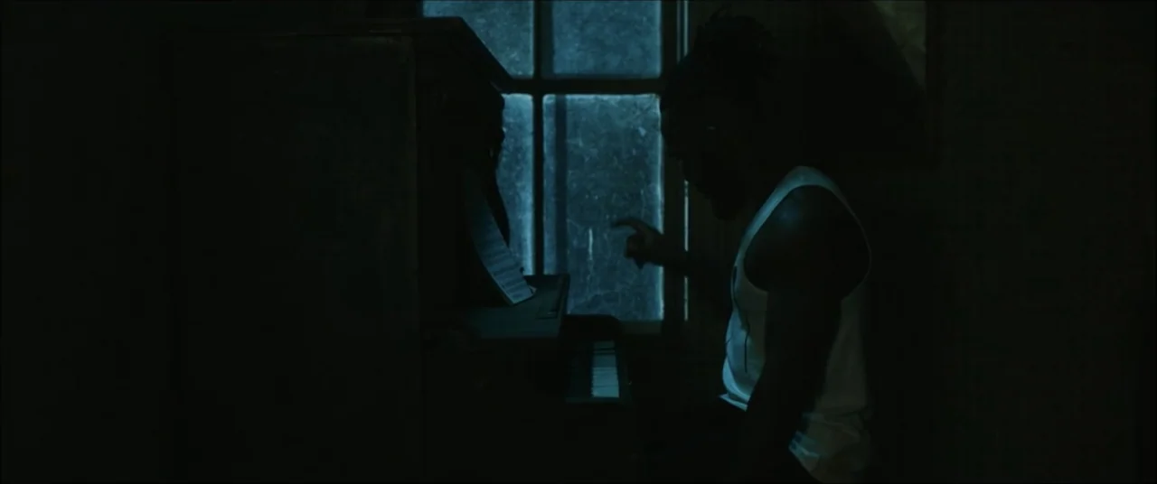 I'll Take Your Dead (2018) movie still: medium — A dark, sparsely furnished room features a window with a faint blue light outside. A man in a white…