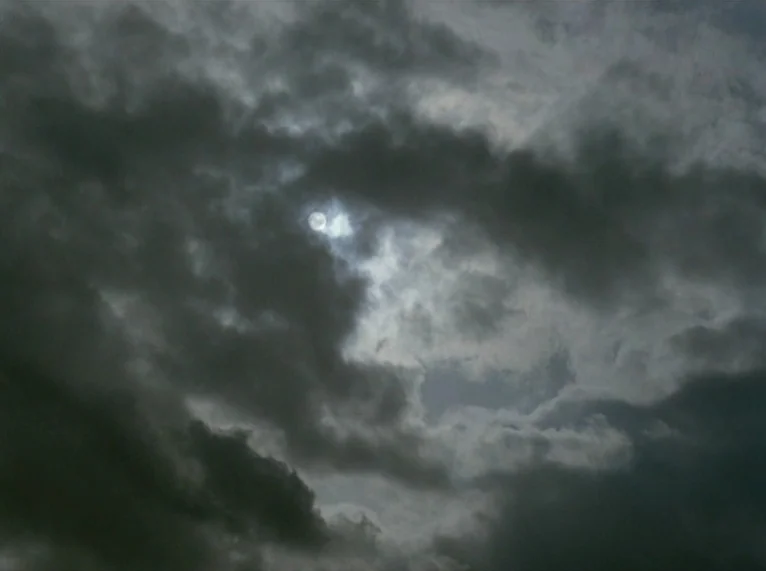 Hail Mary (1985) movie still: establishing — A dense expanse of dark grey cumulus clouds fills the night sky. A single small bright moon is…