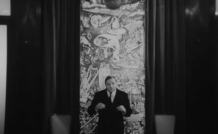 The Cremator (1969) movie still: medium — A man stands before a large, complex monochromatic painting framed by heavy curtains. The composition is…