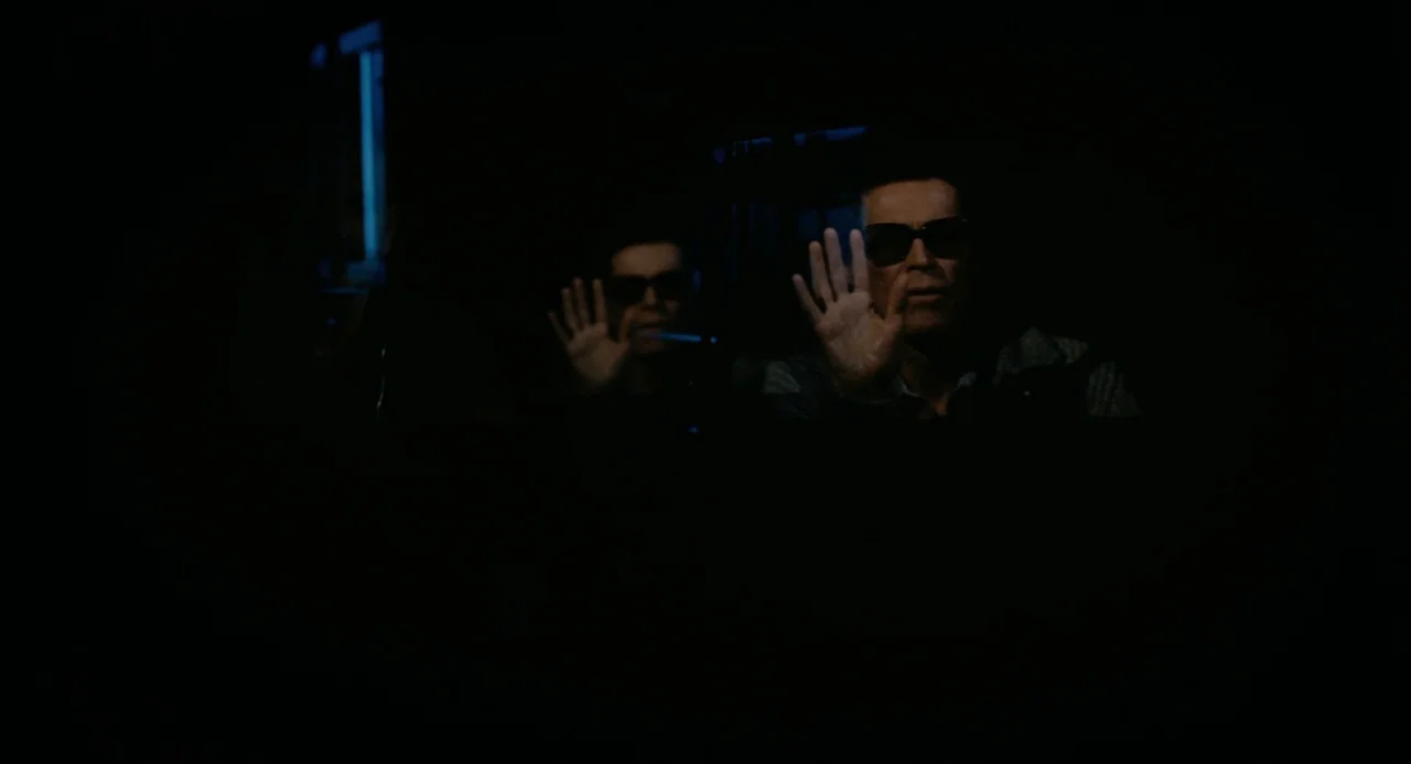 Pasolini (2014) movie still: medium — The interior of a car at night is cast in deep shadow and blue light. Two men sit side by side, holding their…