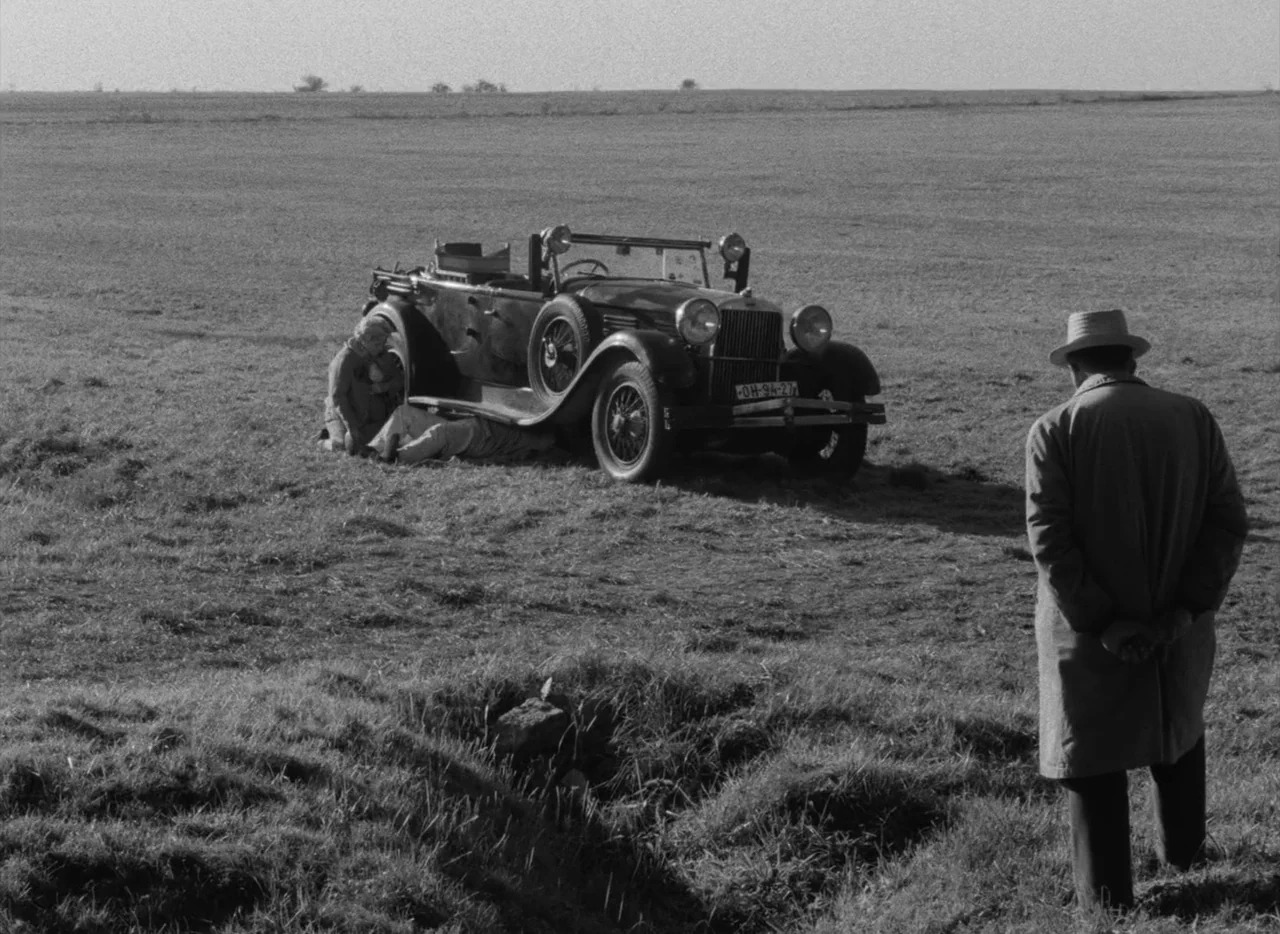 Pearls of the Deep (1965) movie still: wide — A vast, flat, grassy field stretches toward a distant, clear horizon. A vintage open-top car is parked…