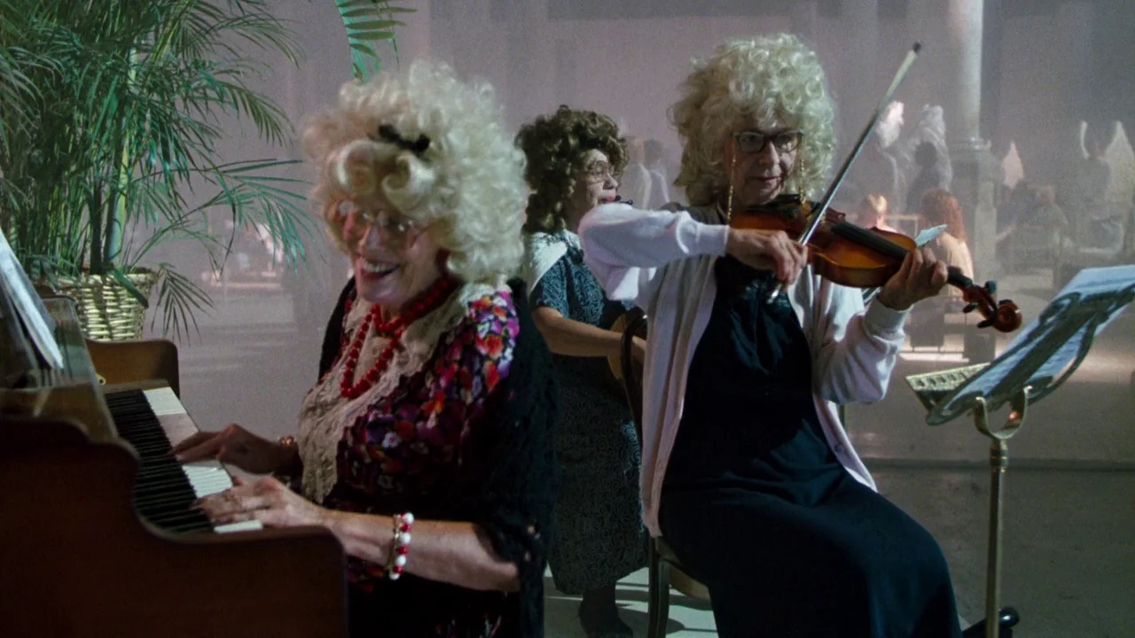 The Exorcist 3 (1990) movie still: medium — A spacious room features a piano, a violin, and a large potted plant. Two older women perform music in…