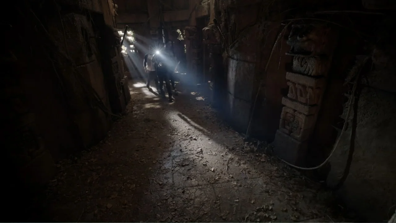 Legends of the Hidden Temple (2016) movie still: wide — An ancient stone corridor features carved pillars and a floor covered in dead leaves. Two…