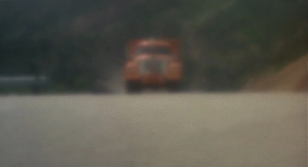 Vanishing Point (1971) movie still: wide — A blurred orange vehicle travels down a dusty road bordered by earth embankments. The camera focus is set…