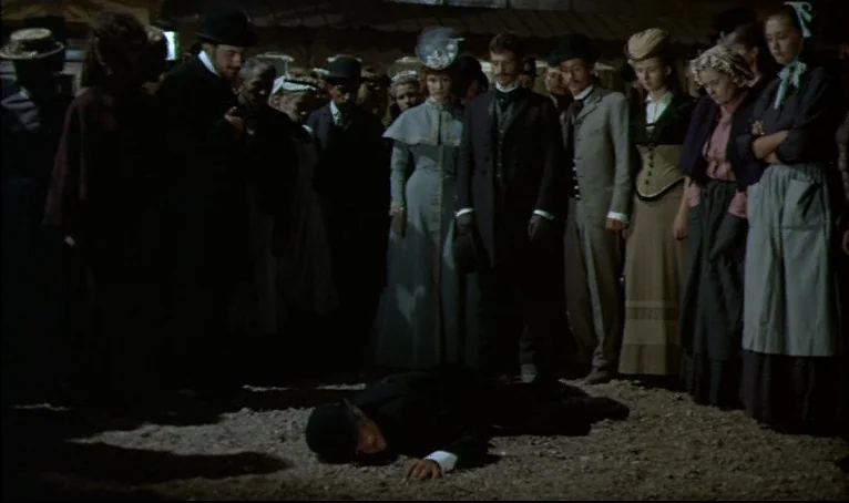 The Thief of Paris (1967) movie still: fullbody — A crowd of people in 19th-century attire stands in a circle on dirt ground. A man in a dark suit…