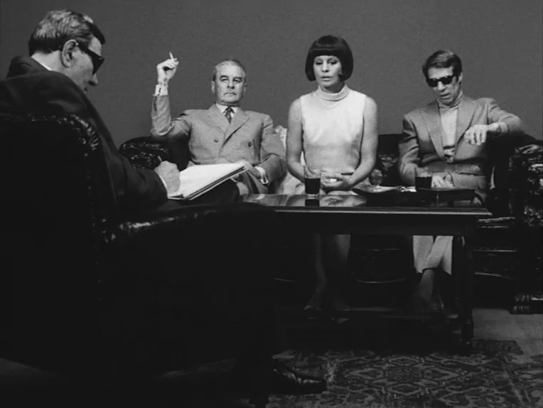 The Rite (1969) movie still: medium — A minimalist studio set features four people seated in a line against a flat background. Three subjects are on…