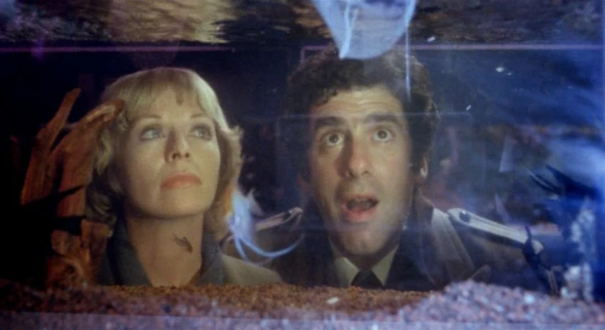 The Silent Partner (1978) movie still: medium — Two people observe the contents of a large glass fish tank. The dimly lit interior reflects off the…