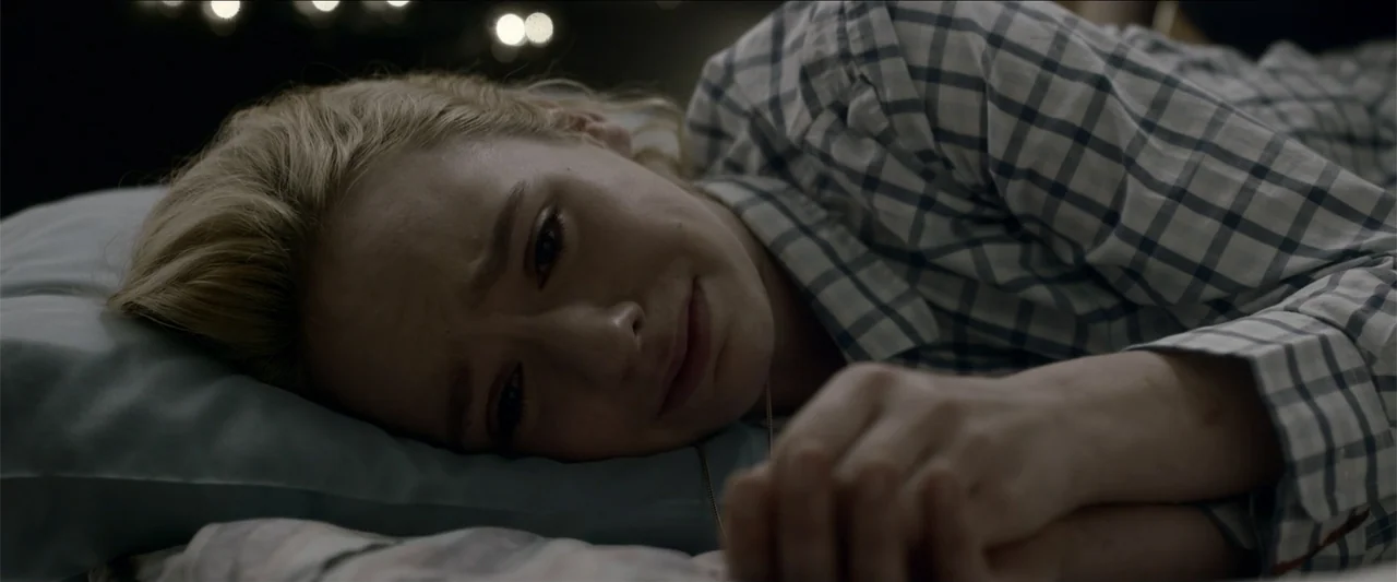 The Hollow Child (2018) movie still: closeup — A dark bedroom interior features a person resting on a blue pillow. The subject lies on their side…