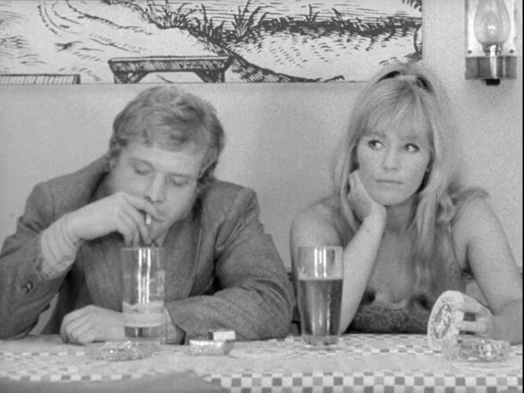 Katzelmacher (1969) movie still: medium — A table in a restaurant with a checkered tablecloth and two filled glasses. The man smokes a cigarette…