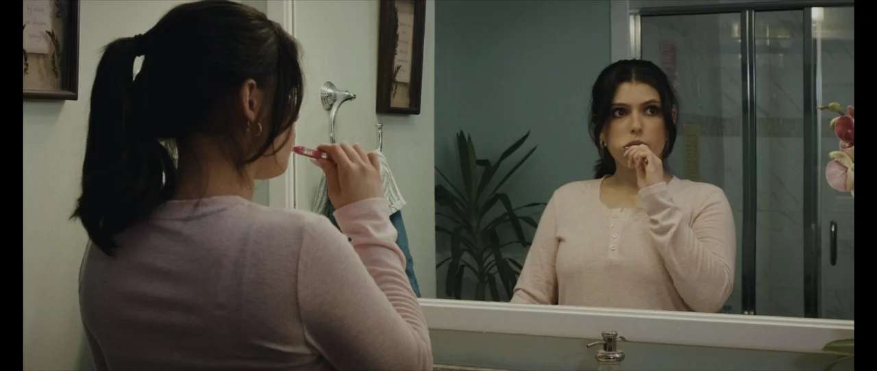 Ordinary Things (2001) movie still: medium — A residential bathroom with pale green walls and a large vanity mirror. A woman in a pink top brushes…
