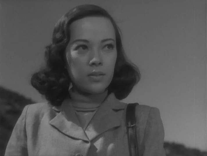 Scandal (1950) movie still: closeup — A woman stands in an outdoor environment with a hilly, barren landscape visible behind. She turns her head…