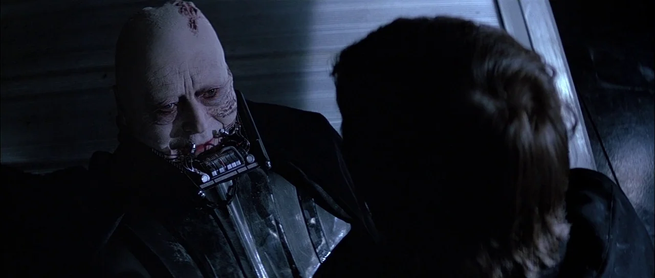Return Of The Jedi (1983) movie still: medium — A dimly lit metallic corridor on a starship with brushed steel wall panels. An elderly, scarred man…