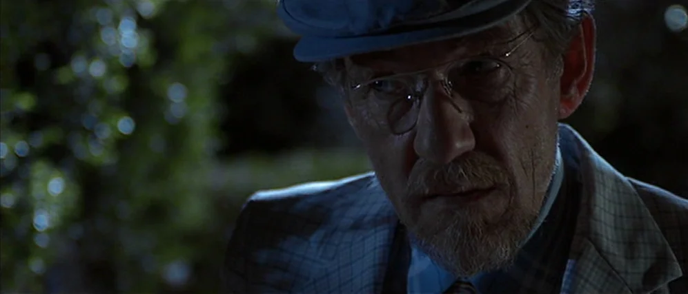 Apt Pupil (1998) movie still: closeup — An older man stands outdoors at night in front of blurred dark vegetation. He wears a plaid jacket and…
