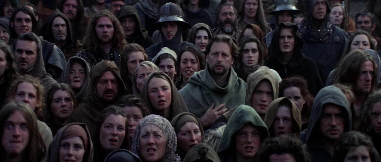 Braveheart (1995) movie still: wide — A dense crowd of people in medieval-style clothing gathers in an outdoor setting. The individuals look toward…