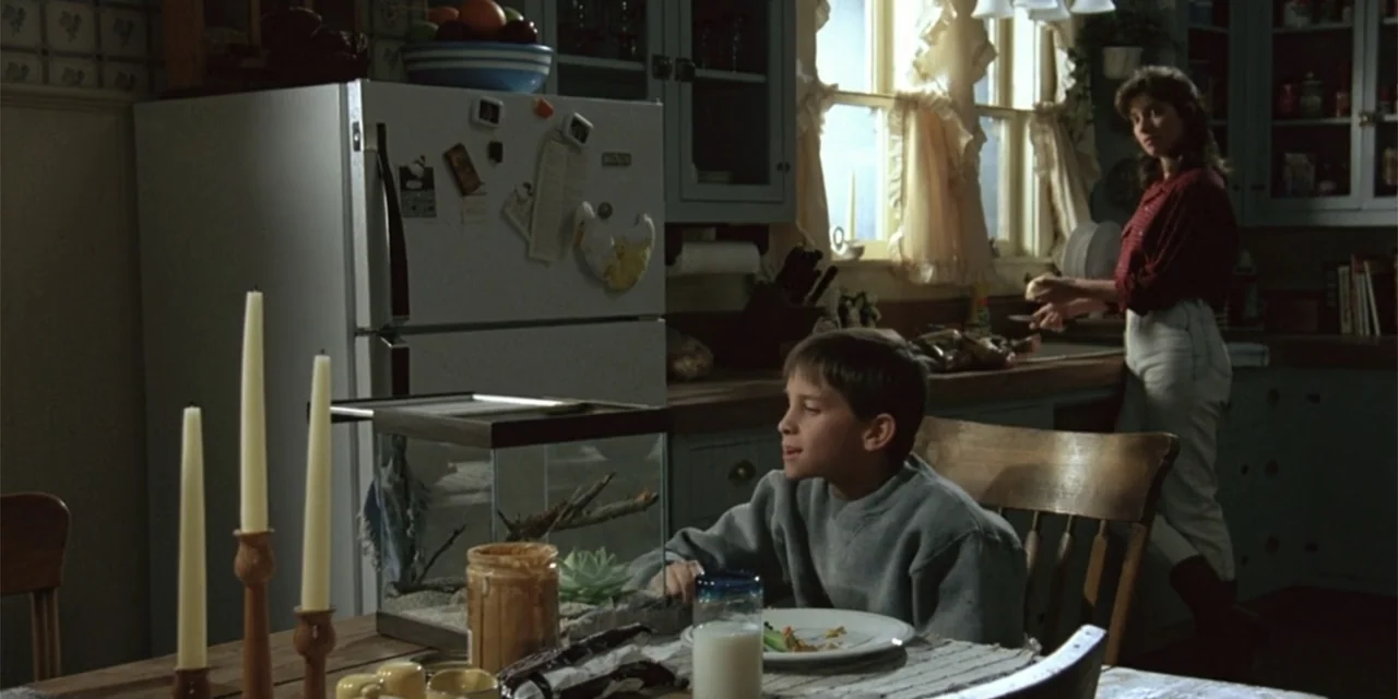 El sótano (2024) movie still: medium — A 1990s-style domestic space features wood cabinets and a refrigerator adorned with various notes. A young…