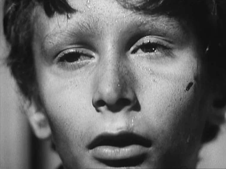 Oliver Twist (1948) movie still: closeup — A close-up shot of a young boy's face in black and white lighting. The boy stares into the distance with…