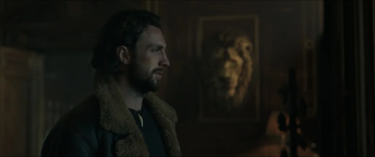 Kraven the Hunter (2024) movie still: medium — A dimly lit room contains a framed lion portrait hanging on a dark wall. A man in a shearling collar…