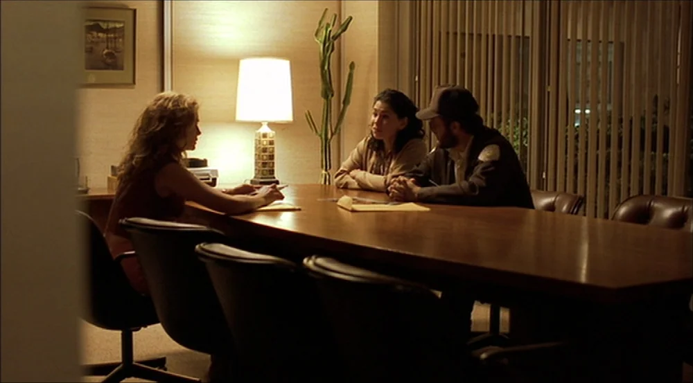 Erin Brockovich (2000) movie still: wide — A dark conference room with beige walls and vertical blinds covers the windows at night. Three people sit…